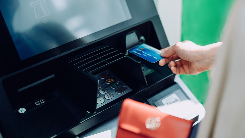 A woman holding a payment card is using an ATM